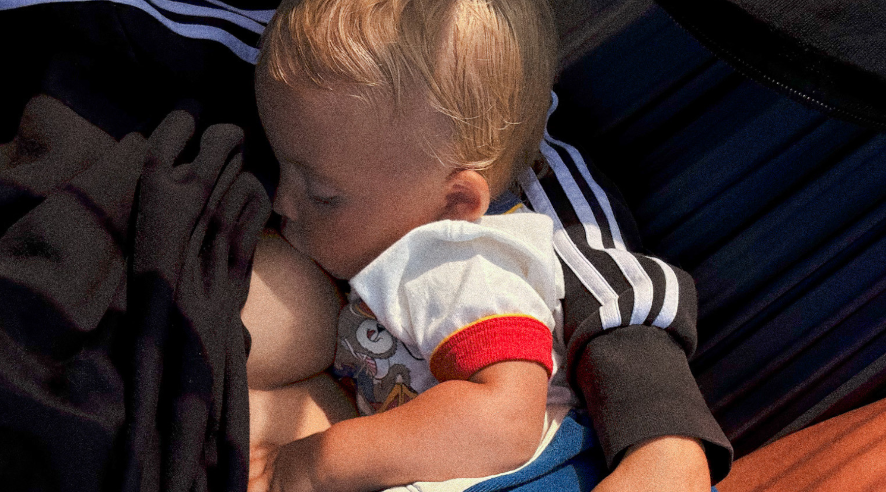 Mother holding nursing baby while napping in the sun. 
