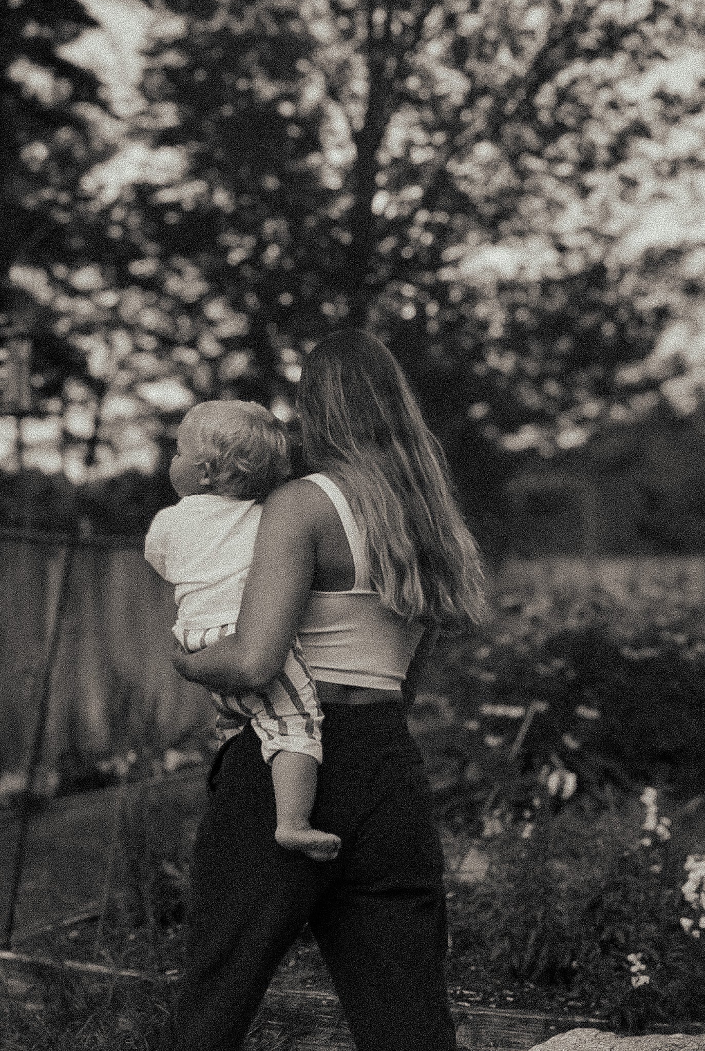 A mother holding her baby outdoors, standing quietly together in a natural setting.